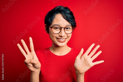 Young beautiful asian girl wearing casual t-shirt and glasses over isolated red background showing and pointing up with fingers number eight while smiling confident and happy.