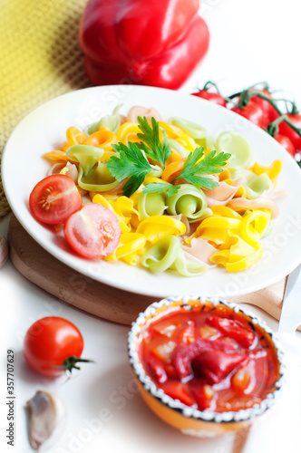 Colorful pasta with tomatoes, garlic, parsley, pepper on a white plate. Pasta for child with tomato sauce on a white background