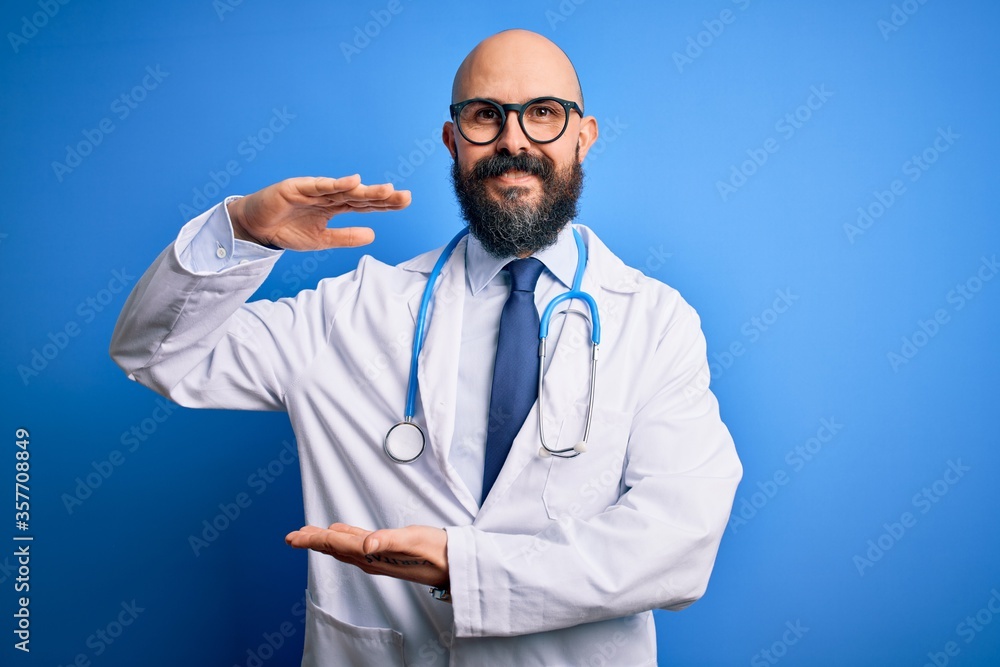 Handsome bald doctor man with beard wearing glasses and stethoscope over blue background gesturing with hands showing big and large size sign, measure symbol. Smiling looking at the camera. Measuring. Handsome bald doctor man with beard wearing glasses and stethoscope over blue background gesturing with hands showing big and large size sign, measure symbol. Smiling looking at the camera. Measuring.