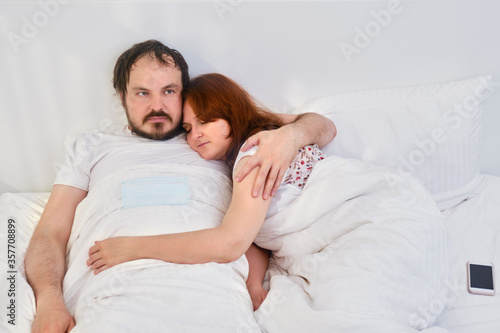 A couple a man and a woman are lying in an embrace in a white bed. Relationship problems coupled with isolation due to coronavirus.
