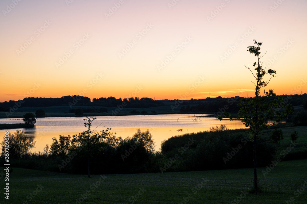 Beautiful rural landscape with a lake, trees and an orange sunset