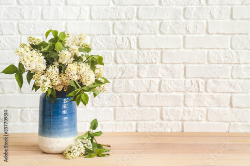 Vase with beautiful flowers on table near white brick wall