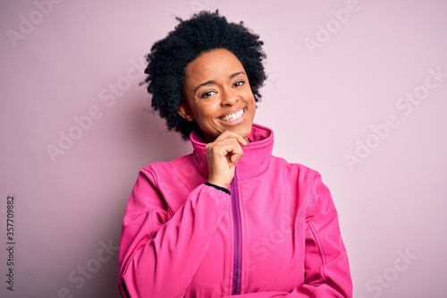 Young African American afro sportswoman with curly hair wearing sportswear doin sport looking confident at the camera with smile with crossed arms and hand raised on chin. Thinking positive.