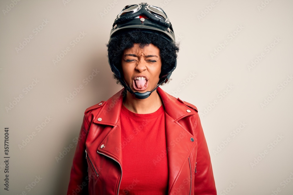 Young African American afro motorcyclist woman with curly hair wearing motorcycle helmet sticking tongue out happy with funny expression. Emotion concept. Young African American afro motorcyclist woman with curly hair wearing motorcycle helmet sticking tongue out happy with funny expression. Emotion concept.