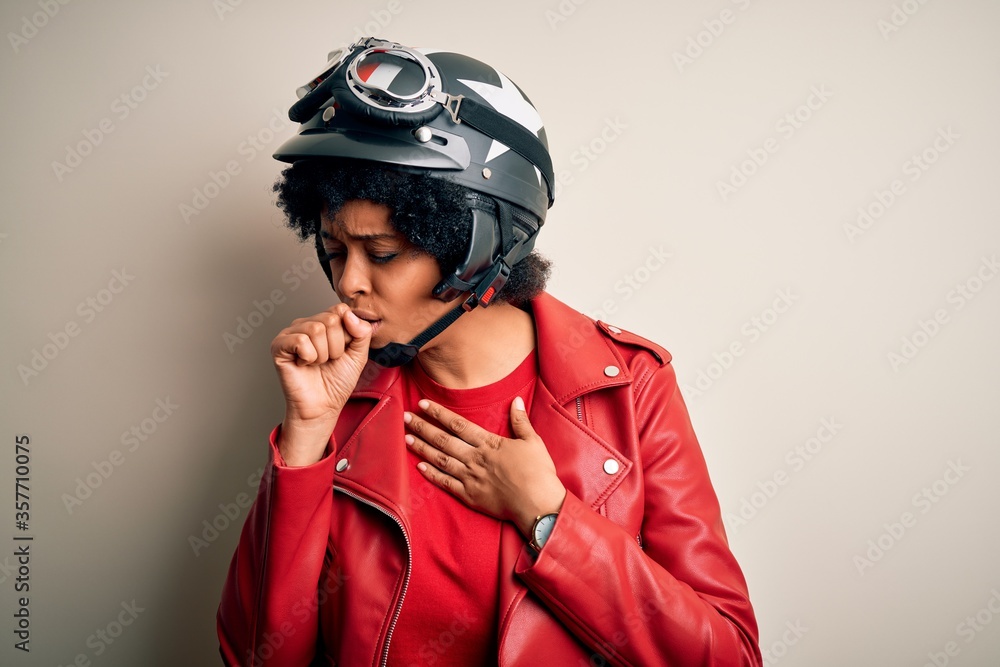 Young African American afro motorcyclist woman with curly hair wearing motorcycle helmet feeling unwell and coughing as symptom for cold or bronchitis. Health care concept. Young African American afro motorcyclist woman with curly hair wearing motorcycle helmet feeling unwell and coughing as symptom for cold or bronchitis. Health care concept.