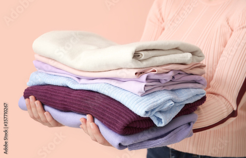 Woman with stack of clean clothes on color background, closeup