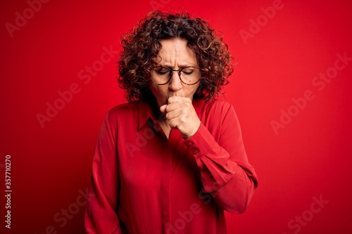 Фотография Middle age beautiful curly hair woman wearing casual shirt and glasses over red background feeling unwell and coughing as symptom for cold or bronchitis