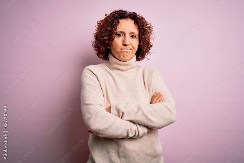 Middle age beautiful curly hair woman wearing casual turtleneck sweater over pink background skeptic and nervous, disapproving expression on face with crossed arms. Negative person. Middle age beautiful curly hair woman wearing casual turtleneck sweater over pink background skeptic and nervous, disapproving expression on face with crossed arms. Negative person.