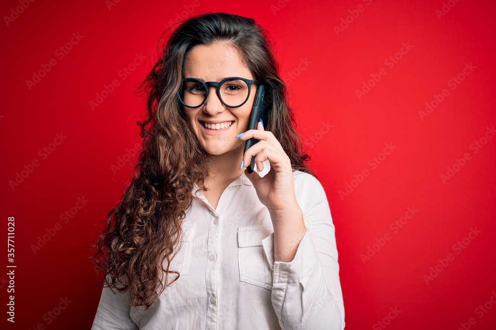 Young beautiful woman with curly hair having conversation talking on the smartphone with a happy face standing and smiling with a confident smile showing teeth Young beautiful woman with curly hair having conversation talking on the smartphone with a happy face standing and smiling with a confident smile showing teeth