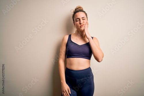 Young beautiful blonde sportswoman doing sport wearing sportswear over white background touching mouth with hand with painful expression because of toothache or dental illness on teeth. Dentist