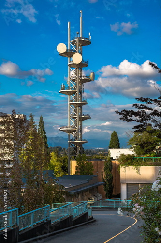 A telecommunications tower located in uptown of New Westminster among buildings and trees against a mountain range and a beautiful cloudy sky. New Westminster City, British Columbia, Canada