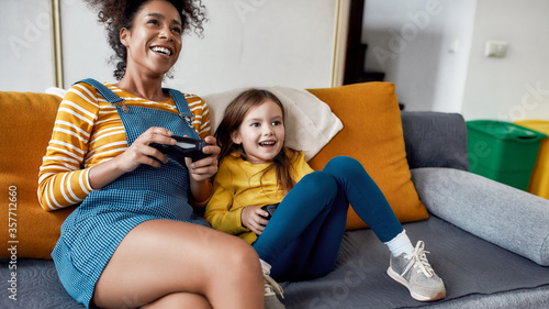 The best care taker. African american woman, baby sitter and little girl having fun together, playing video games, sitting on the couch. Children education, leisure activities, babysitting concept