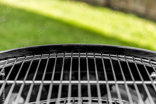 Classic round black BBQ with a clean metal grill shot close up at an angle outside on a sunny day.