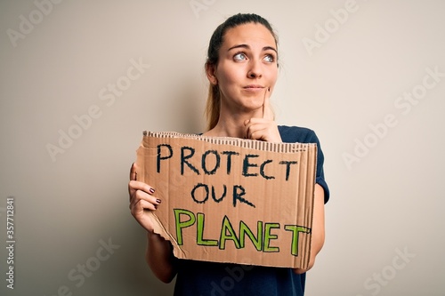 Young beautiful blonde woman with blue eyes asking for protect planet holding banner serious face thinking about question, very confused idea © Krakenimages.com