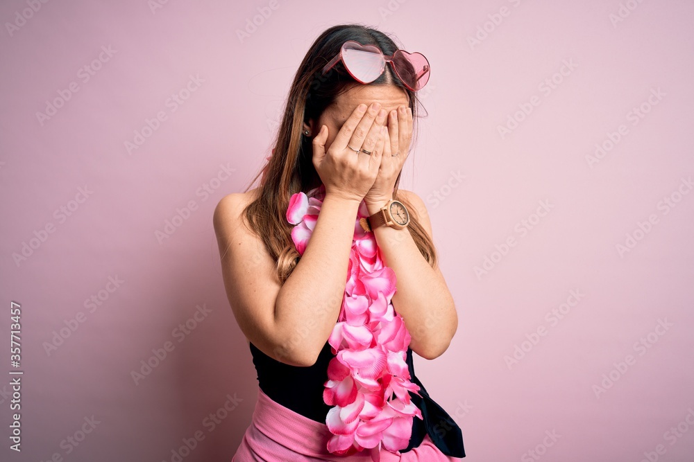 Young beautiful blonde woman wearing swimsuit and floral Hawaiian lei over pink background with sad expression covering face with hands while crying. Depression concept. Young beautiful blonde woman wearing swimsuit and floral Hawaiian lei over pink background with sad expression covering face with hands while crying. Depression concept.