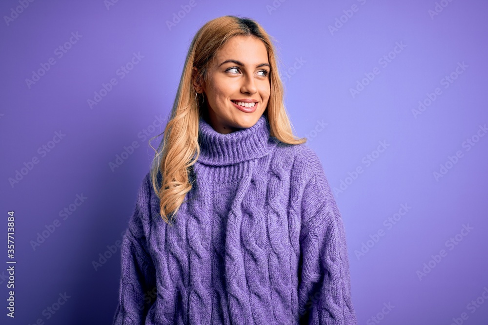 Young beautiful blonde woman wearing casual turtleneck sweater over purple background looking away to side with smile on face, natural expression. Laughing confident. Young beautiful blonde woman wearing casual turtleneck sweater over purple background looking away to side with smile on face, natural expression. Laughing confident.