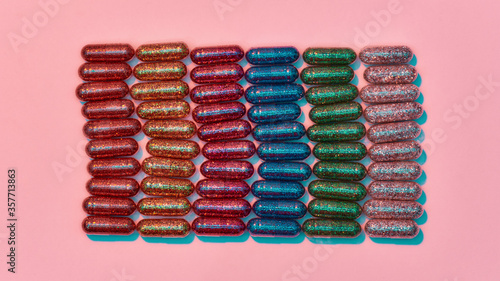 Creative concept with many colorful glitter pills lying in rows isolated on pastel pink background. Minimal style  art concept