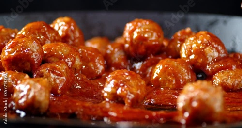Ready meatballs in tomato sauce stirred with a wooden spatula.