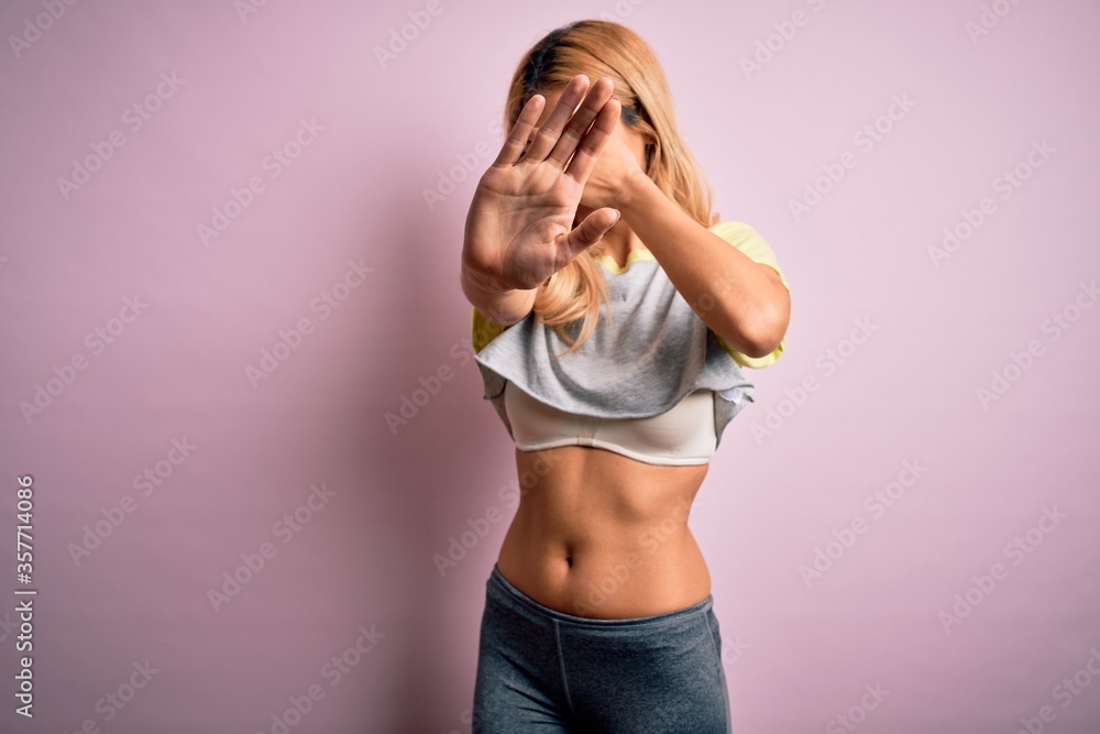 Young beautiful blonde sportswoman doing sport wearing sportswear over pink background covering eyes with hands and doing stop gesture with sad and fear expression. Embarrassed and negative concept. Young beautiful blonde sportswoman doing sport wearing sportswear over pink background covering eyes with hands and doing stop gesture with sad and fear expression. Embarrassed and negative concept.