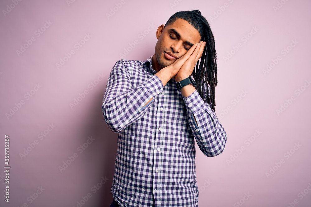 Young handsome african american afro man with dreadlocks wearing casual shirt sleeping tired dreaming and posing with hands together while smiling with closed eyes. Young handsome african american afro man with dreadlocks wearing casual shirt sleeping tired dreaming and posing with hands together while smiling with closed eyes.