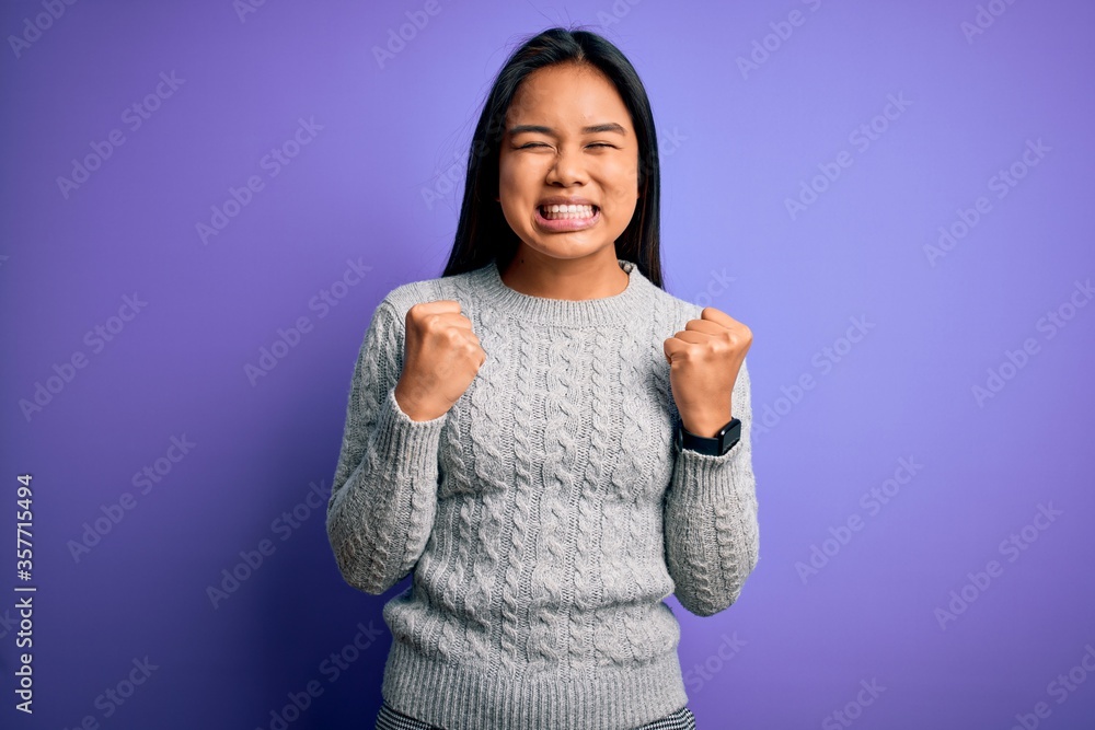 Young beautiful asian girl wearing casual sweater standing over isolated purple background excited for success with arms raised and eyes closed celebrating victory smiling. Winner concept. Young beautiful asian girl wearing casual sweater standing over isolated purple background excited for success with arms raised and eyes closed celebrating victory smiling. Winner concept.