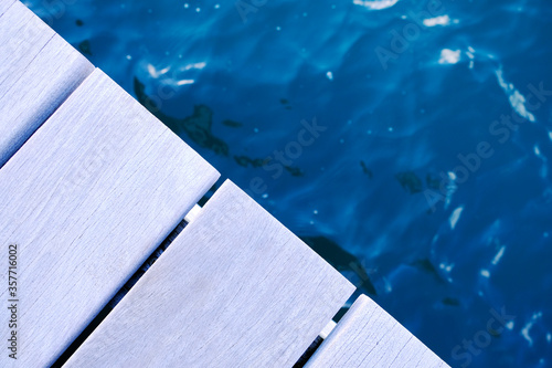 Wooden dock and water in cool evening light, edges of teak planks and blurred dark blue water with reflections.
