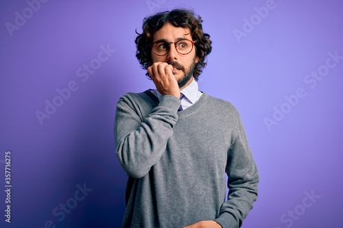 Handsome businessman with beard wearing tie and glasses standing over purple background looking stressed and nervous with hands on mouth biting nails. Anxiety problem.