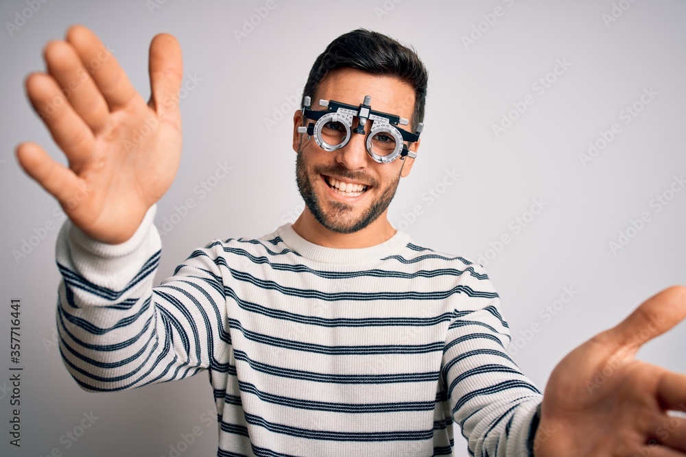 Young handsome man with beard wearing optometry glasses over isolated white background looking at the camera smiling with open arms for hug. Cheerful expression embracing happiness. Young handsome man with beard wearing optometry glasses over isolated white background looking at the camera smiling with open arms for hug. Cheerful expression embracing happiness.