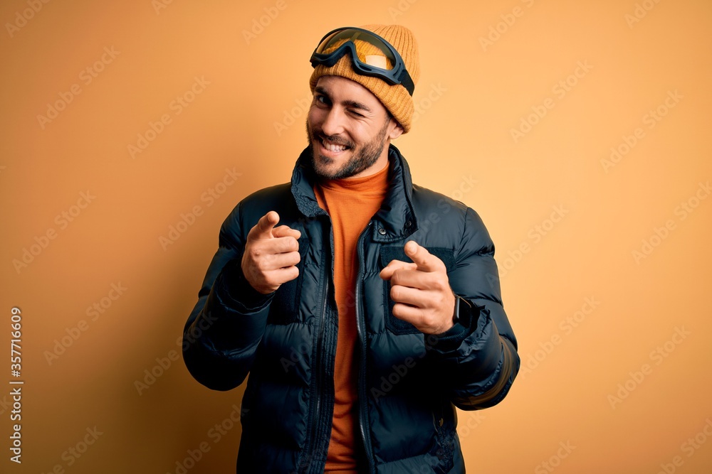 Young handsome skier man with beard wearing snow sportswear and ski goggles pointing fingers to camera with happy and funny face. Good energy and vibes. Young handsome skier man with beard wearing snow sportswear and ski goggles pointing fingers to camera with happy and funny face. Good energy and vibes.