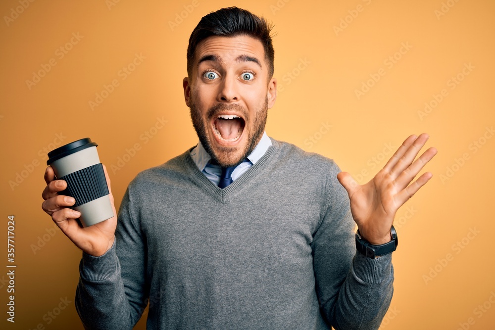Young handsome man drinking a hot coffee from take away plastic cup over yellow background very happy and excited, winner expression celebrating victory screaming with big smile and raised hands Young handsome man drinking a hot coffee from take away plastic cup over yellow background very happy and excited, winner expression celebrating victory screaming with big smile and raised hands