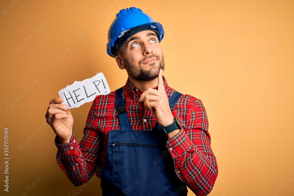 Young builder man wearing safety helmet offering help and support over yellow background serious face thinking about question, very confused idea Young builder man wearing safety helmet offering help and support over yellow background serious face thinking about question, very confused idea