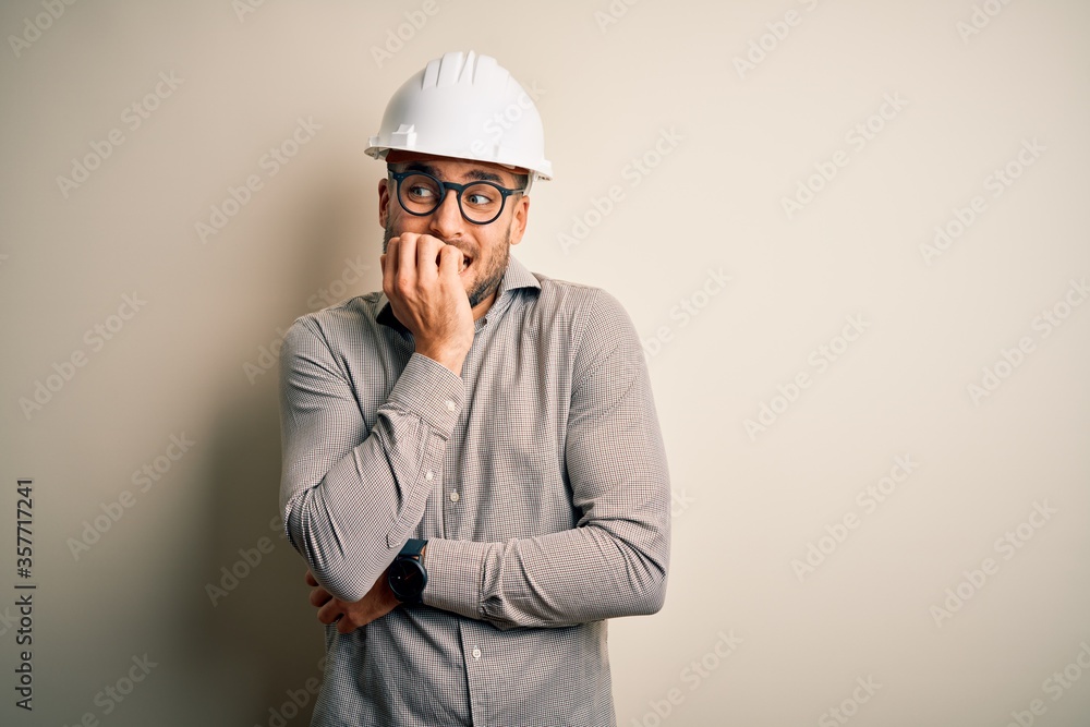 Young architect man wearing builder safety helmet over isolated background looking stressed and nervous with hands on mouth biting nails. Anxiety problem. Young architect man wearing builder safety helmet over isolated background looking stressed and nervous with hands on mouth biting nails. Anxiety problem.