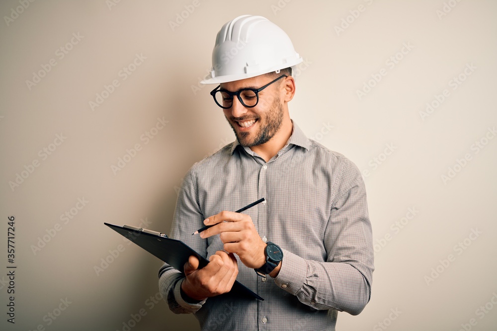 Young architect inspector man wearing builder safety helmet and using clipboard with a happy face standing and smiling with a confident smile showing teeth Young architect inspector man wearing builder safety helmet and using clipboard with a happy face standing and smiling with a confident smile showing teeth