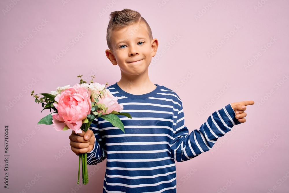 Young little caucasian kid holding romantic and cute bouquet of flowers over pink background very happy pointing with hand and finger to the side Young little caucasian kid holding romantic and cute bouquet of flowers over pink background very happy pointing with hand and finger to the side