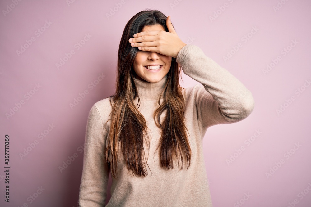 Young beautiful girl wearing casual turtleneck sweater standing over isolated pink background smiling and laughing with hand on face covering eyes for surprise. Blind concept. Young beautiful girl wearing casual turtleneck sweater standing over isolated pink background smiling and laughing with hand on face covering eyes for surprise. Blind concept.