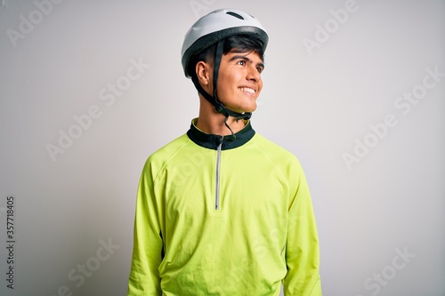 Young handsome cyclist man wearing security bike helmet over isolated white background looking away to side with smile on face, natural expression. Laughing confident.