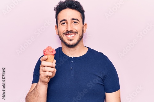 Young hispanic man holding ice cream looking positive and happy standing and smiling with a confident smile showing teeth