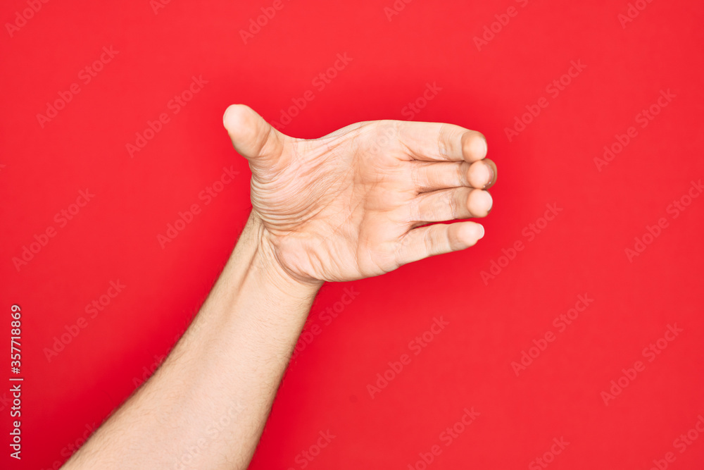 Hand of caucasian young man showing fingers over isolated red background holding invisible object, empty hand doing clipping and grabbing gesture Hand of caucasian young man showing fingers over isolated red background holding invisible object, empty hand doing clipping and grabbing gesture