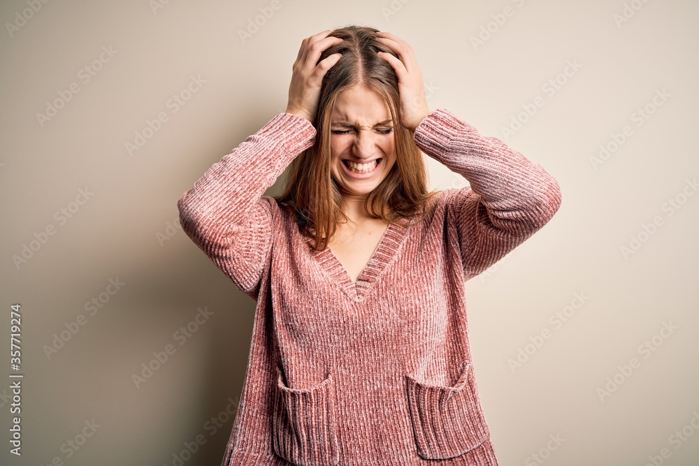 Young beautiful redhead woman wearing pink casual sweater over isolated white background suffering from headache desperate and stressed because pain and migraine. Hands on head. Young beautiful redhead woman wearing pink casual sweater over isolated white background suffering from headache desperate and stressed because pain and migraine. Hands on head.