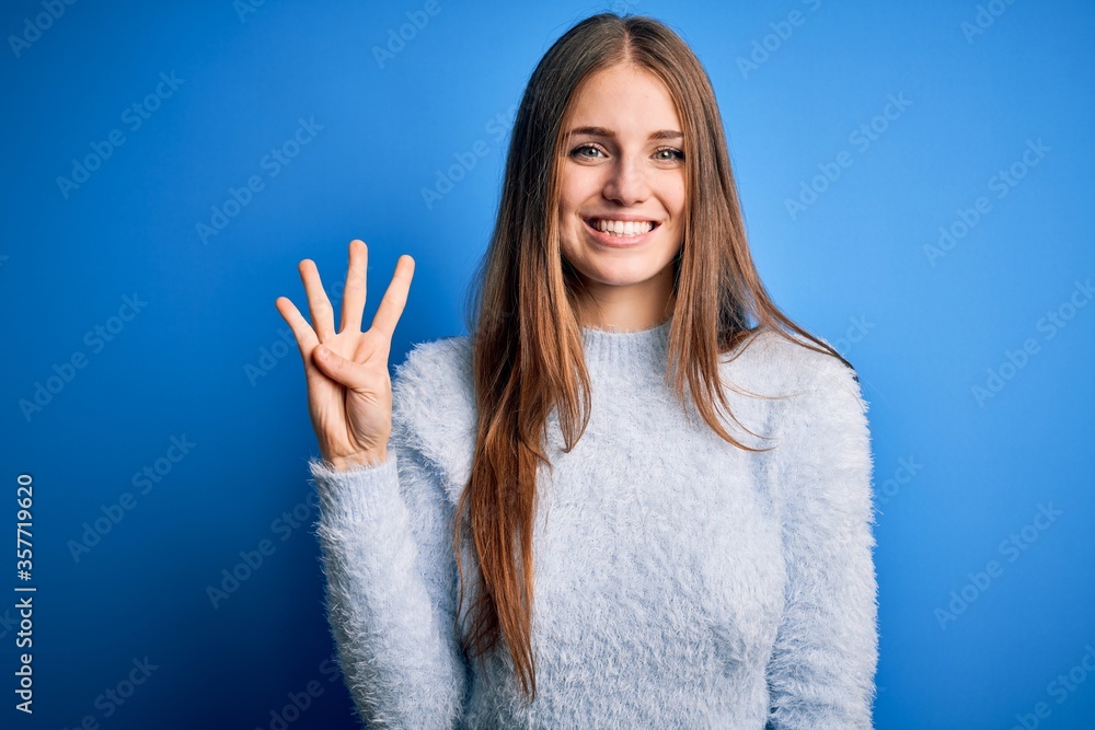 Young beautiful redhead woman wearing casual sweater over isolated blue background showing and pointing up with fingers number four while smiling confident and happy. Young beautiful redhead woman wearing casual sweater over isolated blue background showing and pointing up with fingers number four while smiling confident and happy.