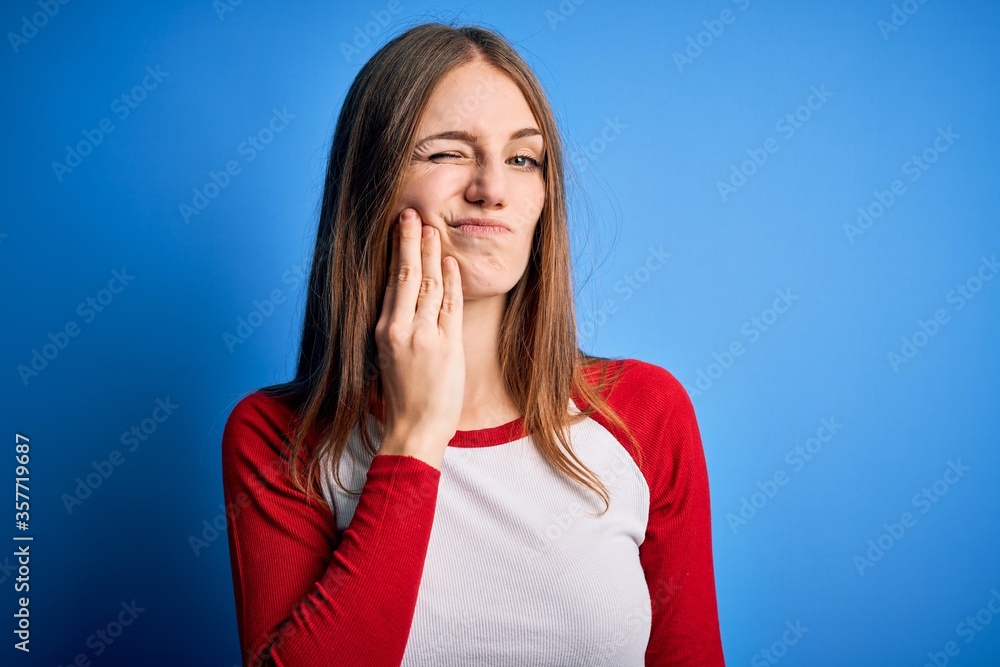 Young beautiful redhead woman wearing casual t-shirt over isolated blue background touching mouth with hand with painful expression because of toothache or dental illness on teeth. Dentist Young beautiful redhead woman wearing casual t-shirt over isolated blue background touching mouth with hand with painful expression because of toothache or dental illness on teeth. Dentist