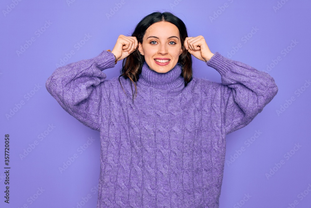 Young beautiful woman wearing casual turtleneck sweater standing over purple background Smiling pulling ears with fingers, funny gesture. Audition problem Young beautiful woman wearing casual turtleneck sweater standing over purple background Smiling pulling ears with fingers, funny gesture. Audition problem