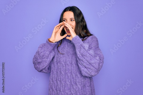 Young beautiful woman wearing casual turtleneck sweater standing over purple background Shouting angry out loud with hands over mouth