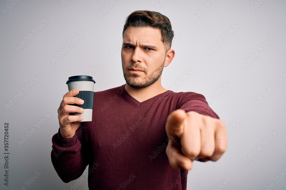 Young man with blue eyes drinking coffee from take away plastic bottle over isolated background pointing with finger to the camera and to you, hand sign, positive and confident gesture from the front Young man with blue eyes drinking coffee from take away plastic bottle over isolated background pointing with finger to the camera and to you, hand sign, positive and confident gesture from the front