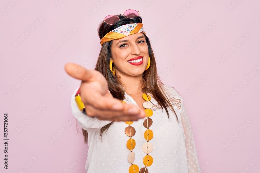 Young hispanic hippie woman wearing fashion boho style and sunglasses over pink background smiling cheerful offering palm hand giving assistance and acceptance. Young hispanic hippie woman wearing fashion boho style and sunglasses over pink background smiling cheerful offering palm hand giving assistance and acceptance.
