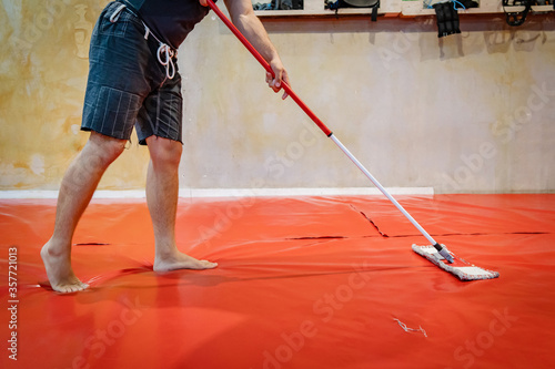 Unknown caucasian man cleaning tatami mats at MMA or BJJ or Judo wrestling  martial arts gym using mop to swipe and disinfect due to coronavirus  pandemic or bacteria fungus preventing infection Stock