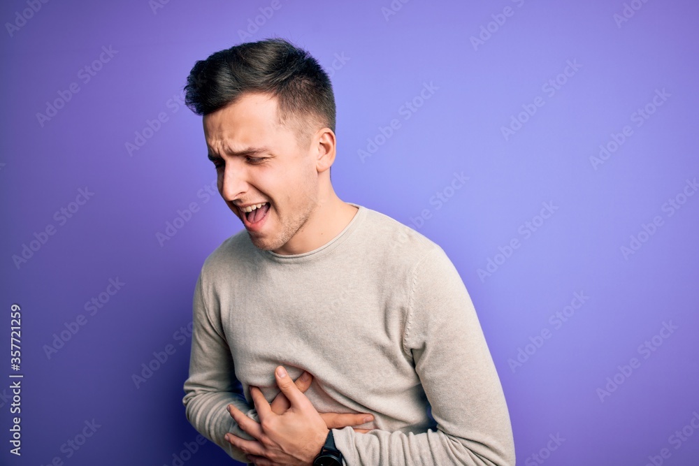 Obraz premium Young handsome caucasian man wearing casual sweater over purple isolated background with hand on stomach because nausea, painful disease feeling unwell. Ache concept.