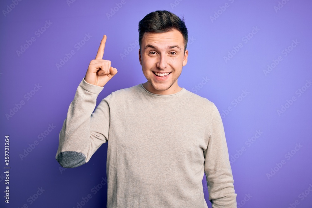 Young handsome caucasian man wearing casual sweater over purple isolated background pointing finger up with successful idea. Exited and happy. Number one. Young handsome caucasian man wearing casual sweater over purple isolated background pointing finger up with successful idea. Exited and happy. Number one.