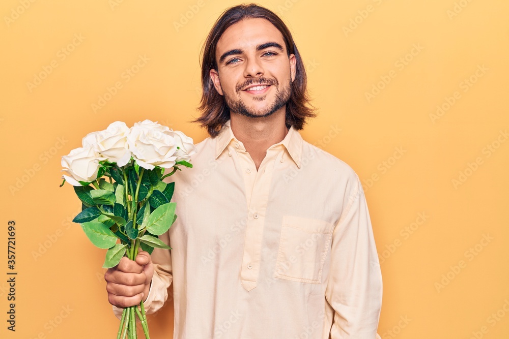 Young handsome man holding flowers looking positive and happy standing and smiling with a confident smile showing teeth Young handsome man holding flowers looking positive and happy standing and smiling with a confident smile showing teeth