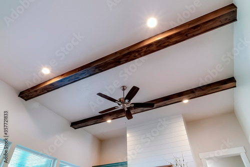 Ceiling fan with lights flanked by decorative wood beams and recessed lighting